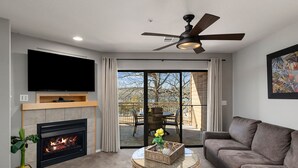A living room with a fireplace, a flat-screen TV, a ceiling fan, and a balcony with outdoor seating. - Still Waters Resort (Branson)