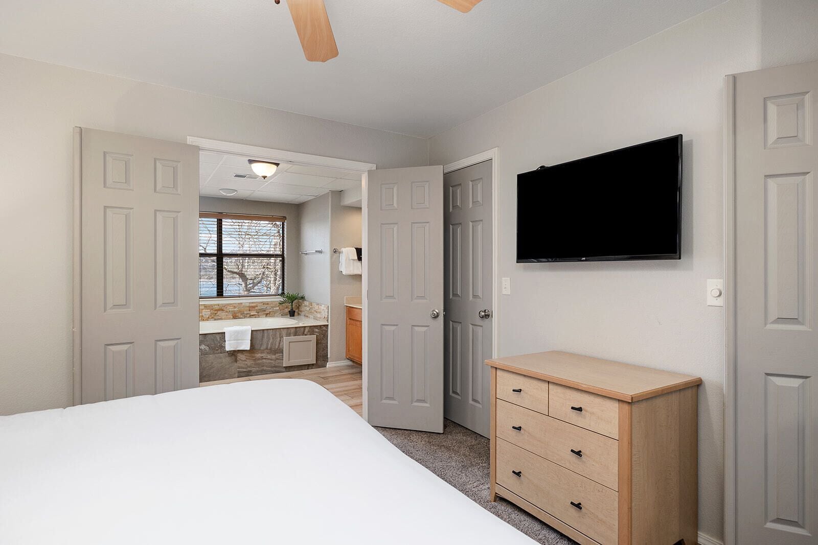 Quarto com cama, penteadeira, televisão e banheiro visível por uma porta aberta.