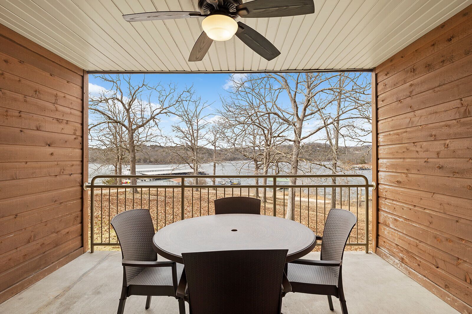 A balcony with a round table and four chairs, overlooking a body of water and trees.