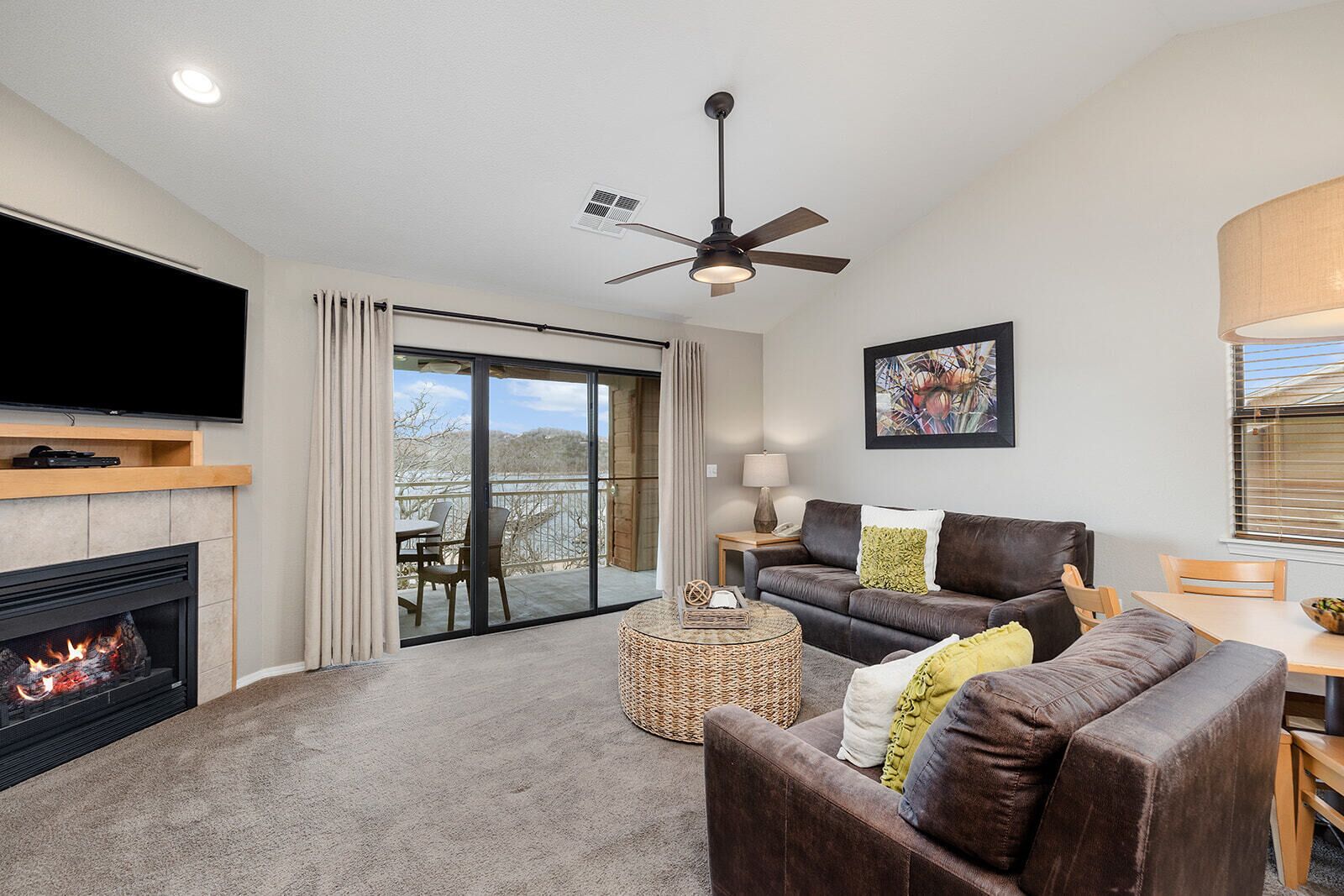 A living room with a fireplace, a television, a sofa, a coffee table, and a balcony with a view.