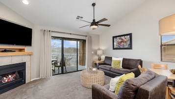 A living room with a fireplace, a television, a sofa, a coffee table, and a balcony with a view.