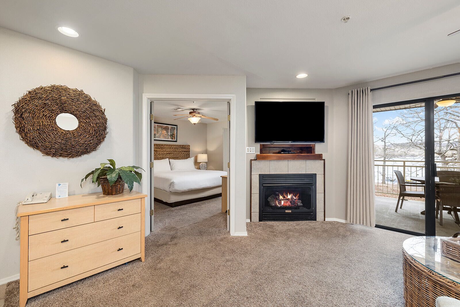 A hotel room with a bed, a fireplace, a television, a wicker table, and a balcony with a view.