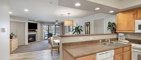 A modern kitchen with wooden cabinets, a built-in dishwasher, and a dining area with a fireplace.