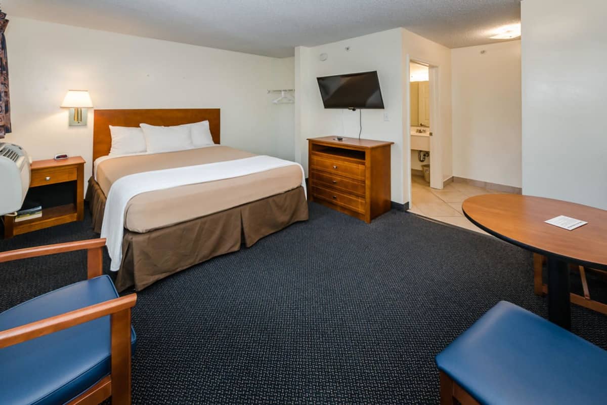 Une chambre d’hôtel avec un lit, un bureau, une chaise, une télévision et une petite table.