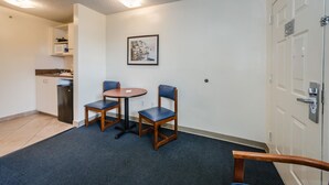A small, clean room with a kitchenette, two chairs, a round table, and a door with a lock.