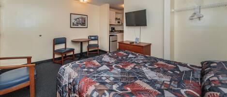 Una habitación de hotel con cama, dos sillones, una mesita, televisión y kitchenette.