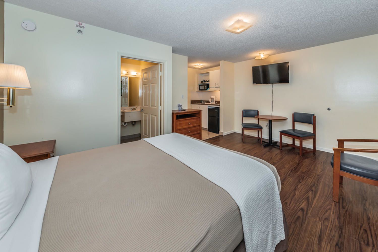 A hotel room with a bed, a desk, a chair, a TV, and a kitchenette.