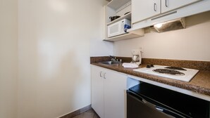 A compact kitchen with white cabinets, a granite countertop, a built-in microwave, a coffee maker, and a dishwasher.
