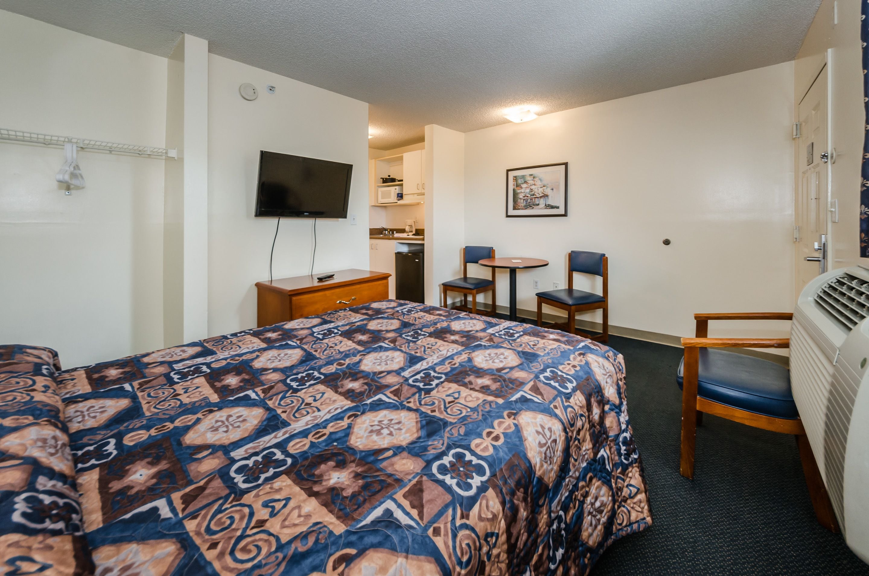 A hotel room with a bed, a desk, a chair, a television, and a kitchenette.