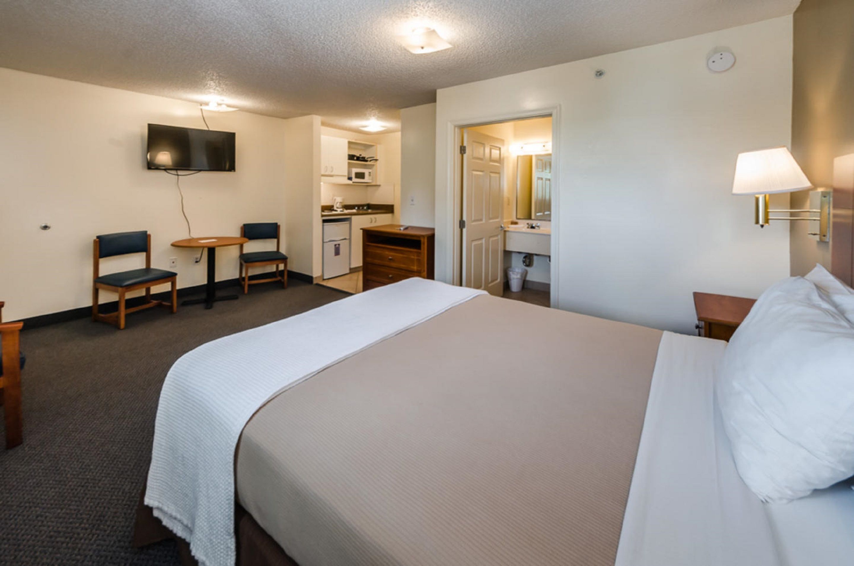 Ein Hotelzimmer mit einem großen Bett, einem Schreibtisch mit zwei Stühlen, einem Fernseher, einer Mikrowelle und einer kleinen Küchenzeile.
