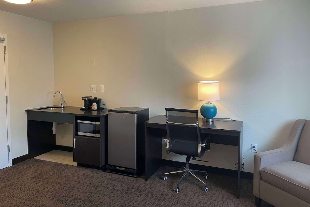 Een compacte hotelkamer met een kitchenette, een bureau met stoel, een lamp en een bank.
