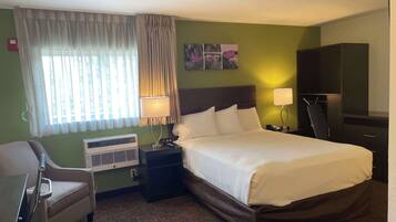Une chambre d’hôtel avec un lit, un bureau, une chaise, une télévision et une fenêtre avec des rideaux.