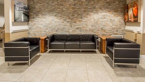 Eine moderne Lobby mit einer Wand aus Steinmosaik, einer schwarzen Ledersofa und zwei schwarzen Sesseln.