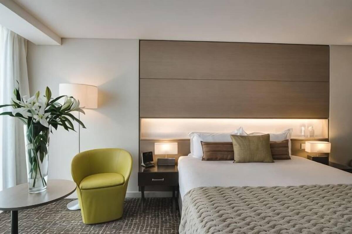 A hotel room with a bed, bedside tables, a lamp, a chair, and a vase with flowers.