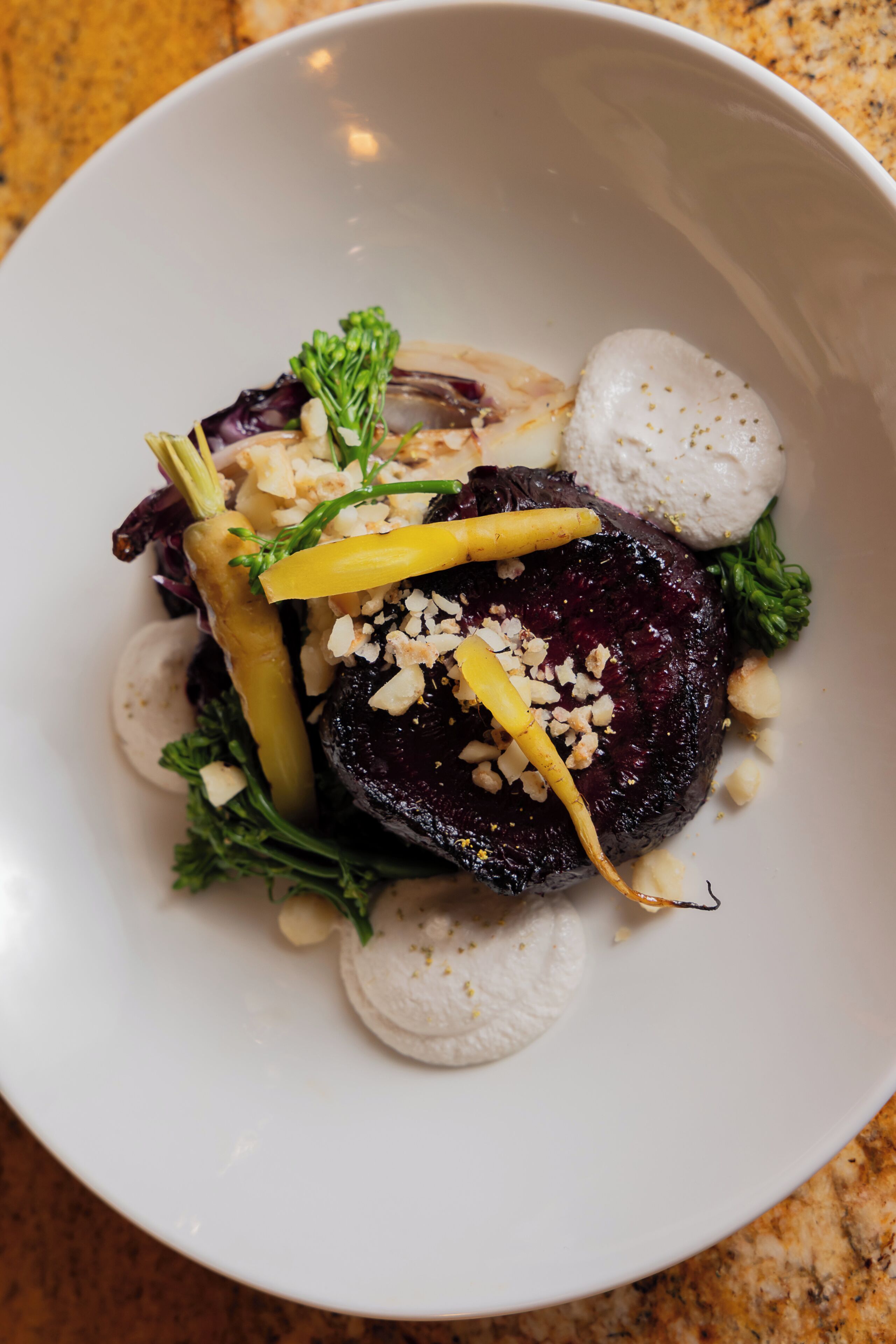 A white plate with a dark-colored meat, vegetables, and a creamy white item, possibly a sauce or garnish.