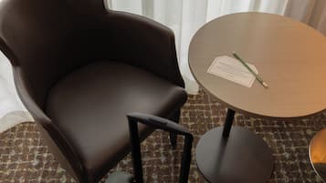 A brown leather chair with a footrest and wheels, a small round table with a document and pencil, and a patterned carpet.