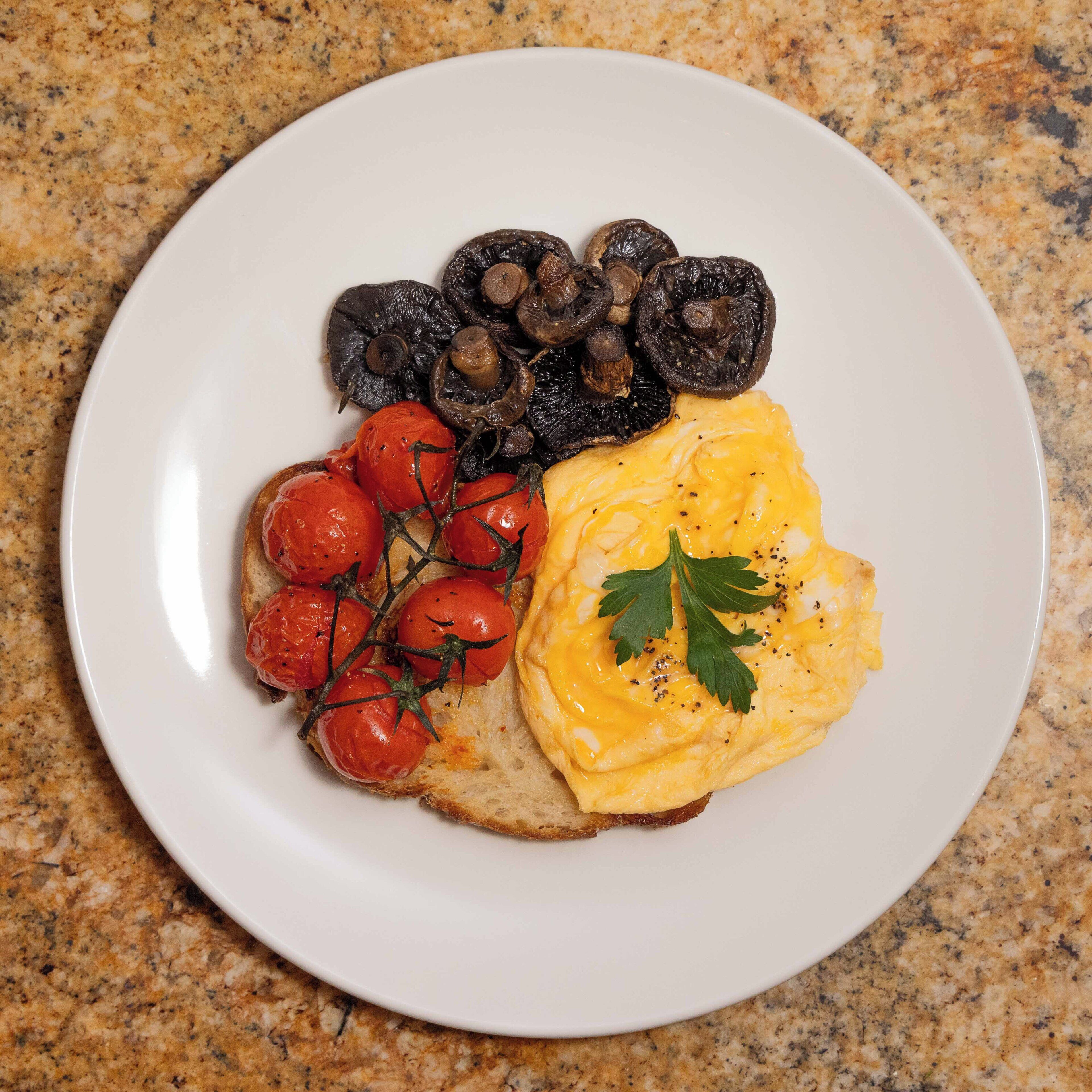 Un plato con huevos revueltos, champiñones asados y tomates cherry sobre tostada.