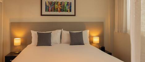 A hotel room with a large bed, two bedside lamps, a framed abstract painting, and a window with curtains.