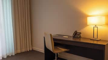 A hotel room with a desk, chair, lamp, phone, and curtains.