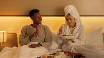 Una habitación de hotel con una cama, almohadas, una lámpara de noche y una bandeja con comida.