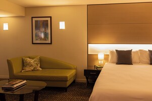 Habitación de hotel con cama, sofá, una mesita con libros, mesita de noche y un cuadro colgado en la pared.