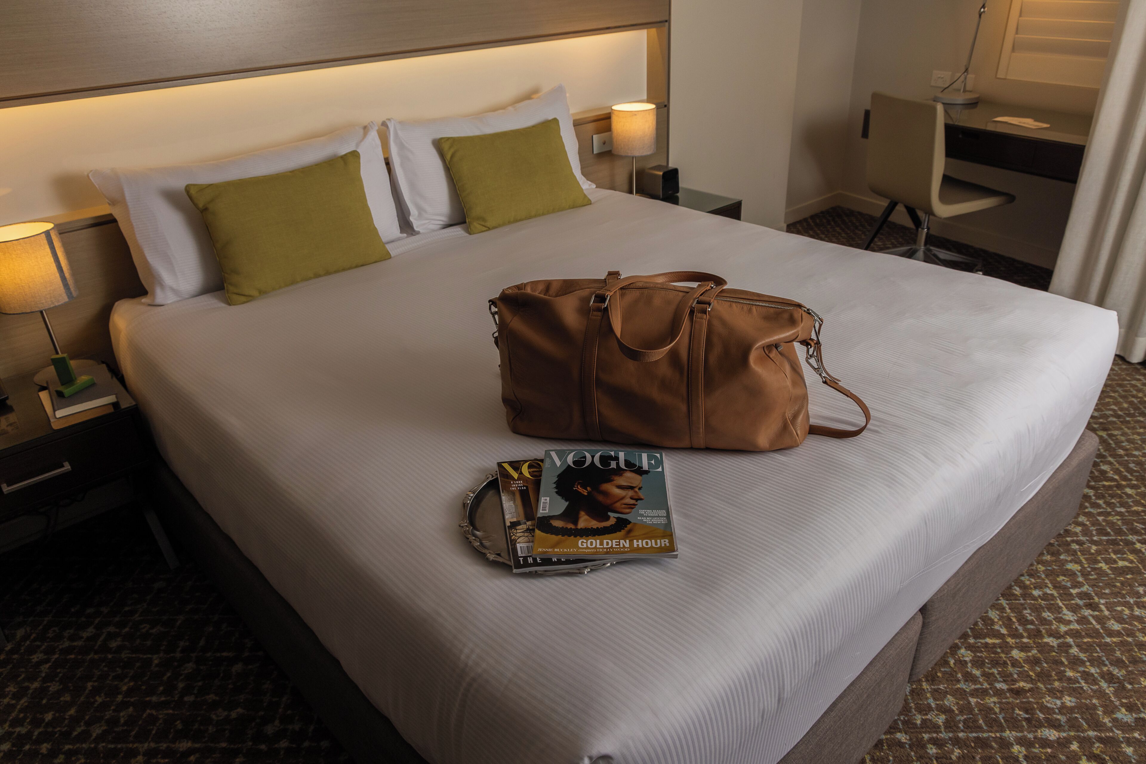 A hotel room with a bed, a nightstand with a lamp, a desk, and a chair.
