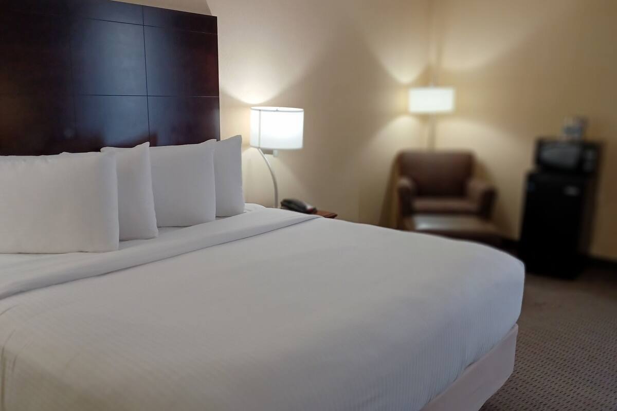 A hotel room with a large bed, a nightstand, a lamp, a chair, and a TV.