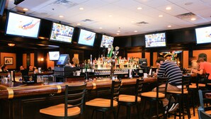 A bar area with multiple screens displaying sports content, bar stools, and a variety of bottles. - Valley Forge Casino Resort (King of Prussia)