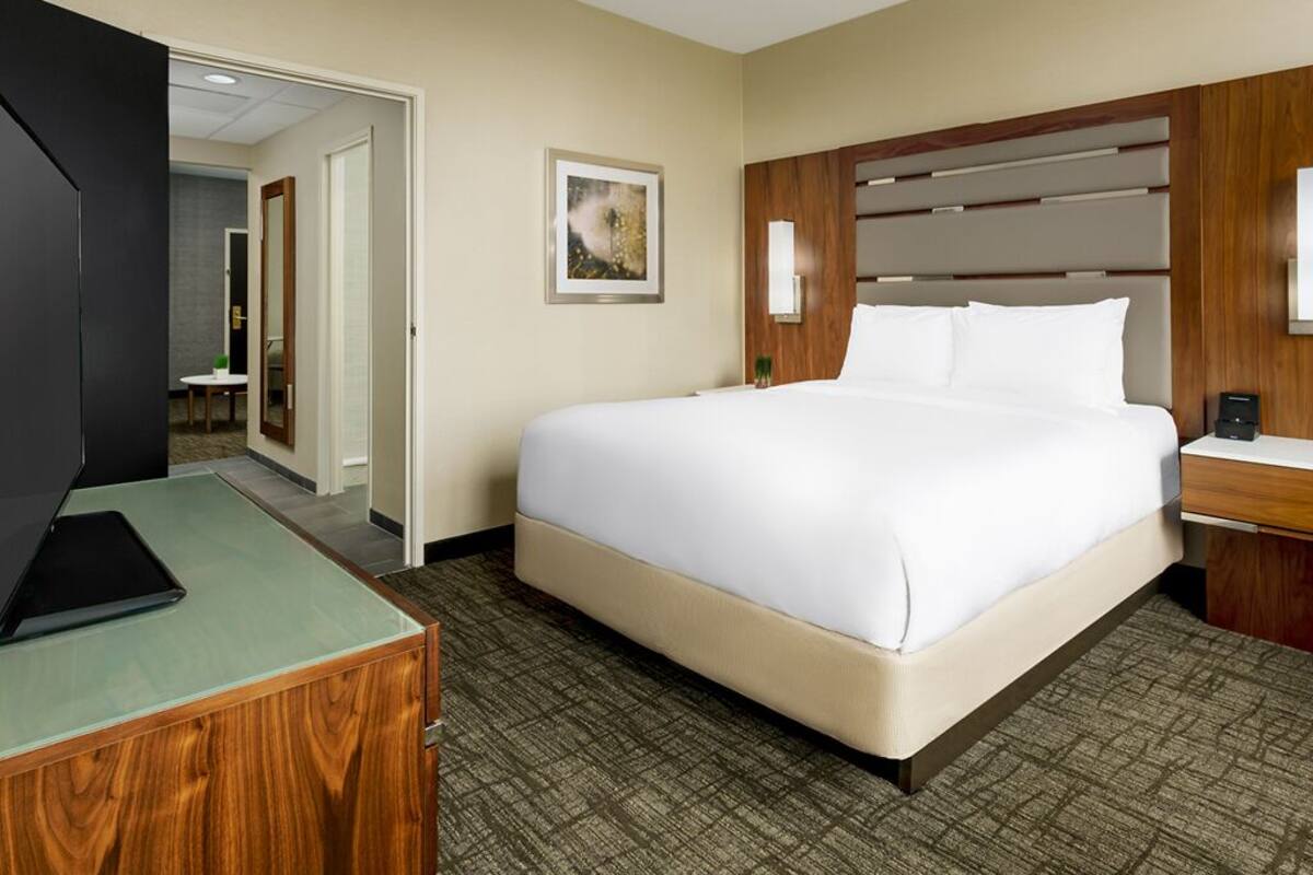 A hotel room with a large bed, a desk with a laptop, a mirror, and a framed picture on the wall.