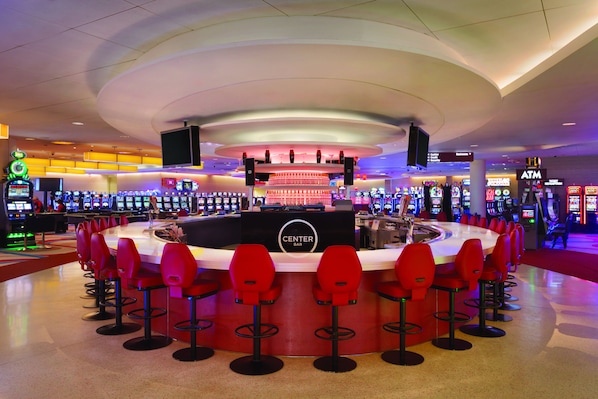 Una zona de bar con distribución circular, múltiples máquinas de juego y taburetes rojos.