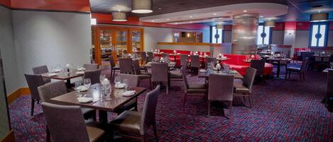 A restaurant with tables set for dining, chairs, and a patterned carpet.