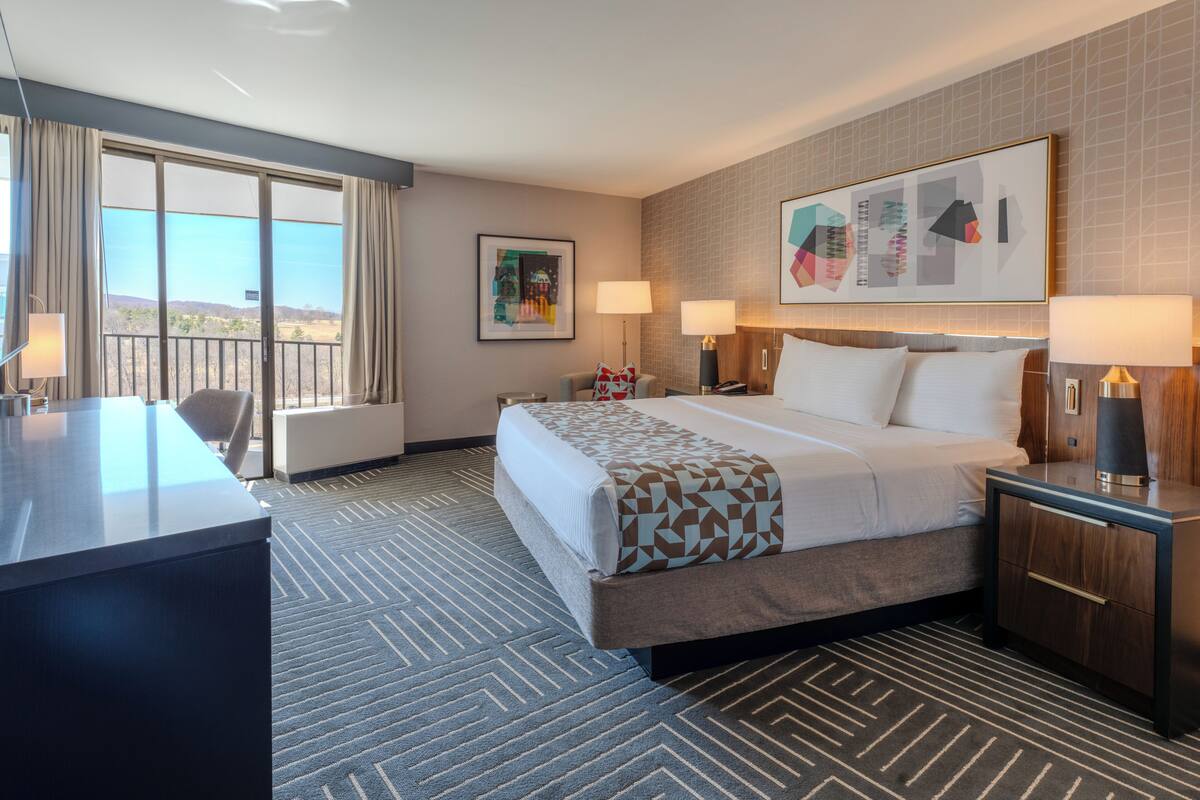 A hotel room with a bed, desk, and large windows.