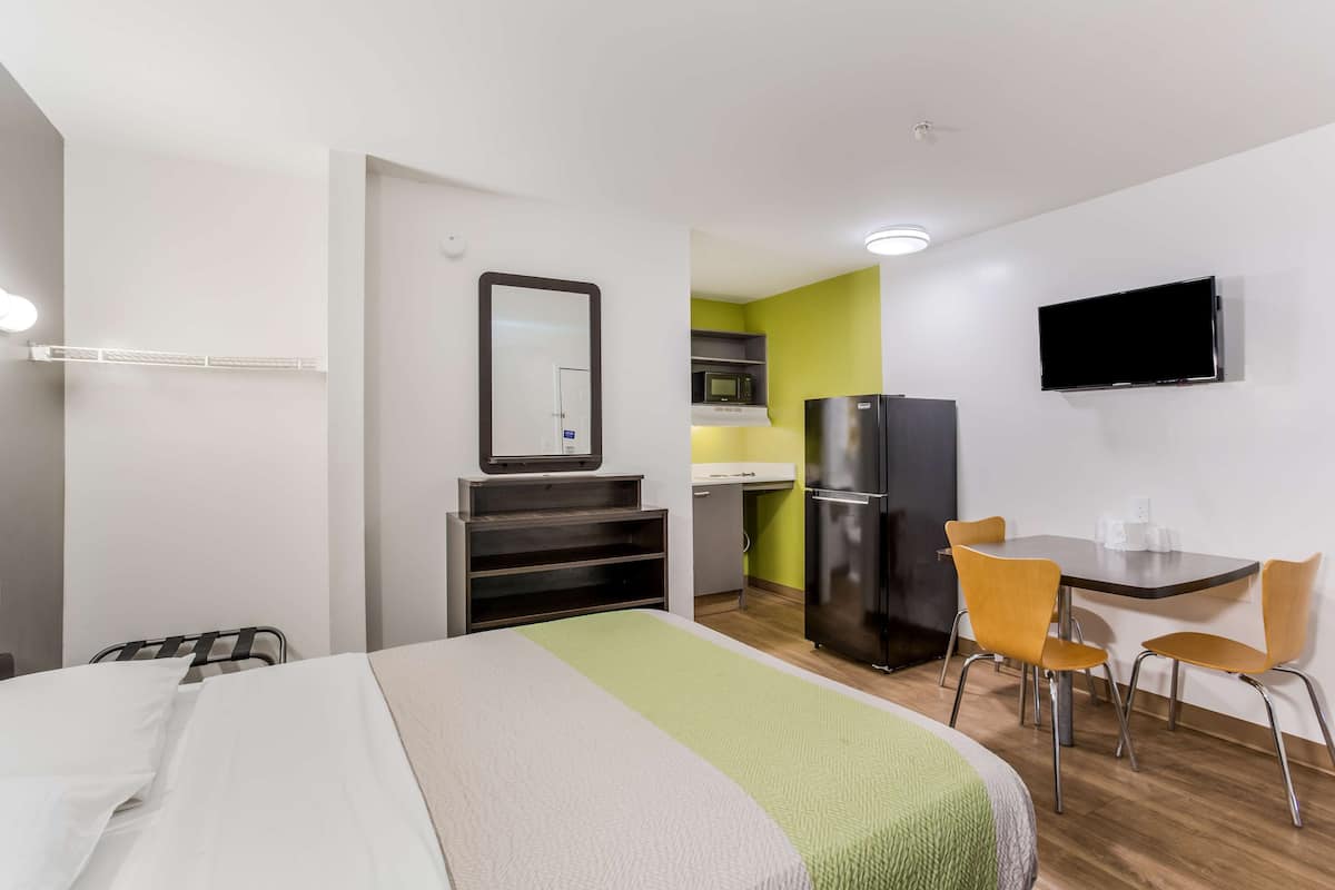 A hotel room with a bed, a desk with chairs, a television, and a kitchenette.