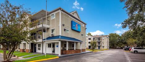 A multi-story hotel with a blue awning, a parking lot, and a clear blue sky.