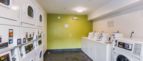 A laundromat with multiple washing machines and dryers, a green wall, and a sign indicating payment options.