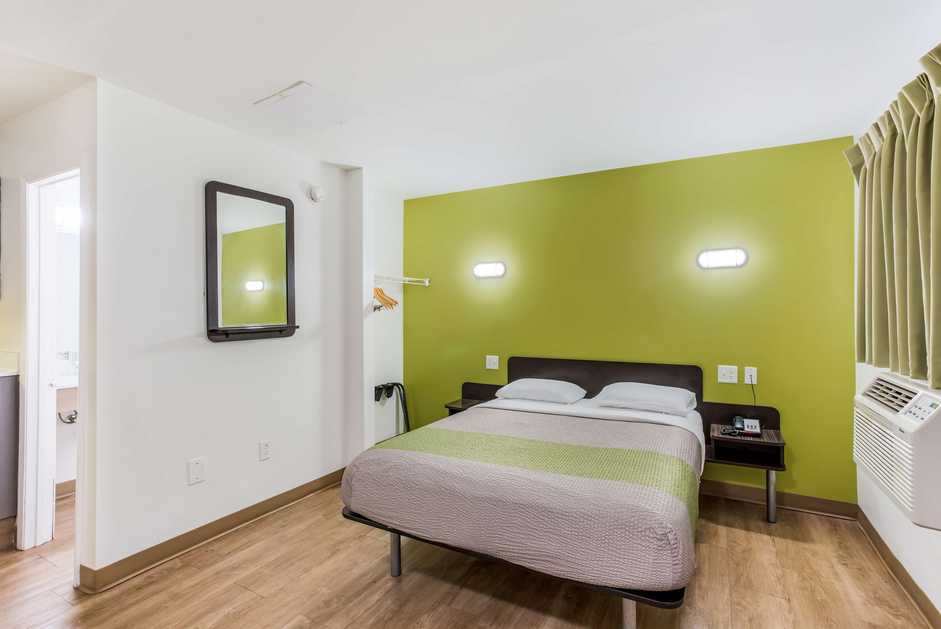 Quarto com cama, mesa de cabeceira, espelho e ar-condicionado fixado na parede.
