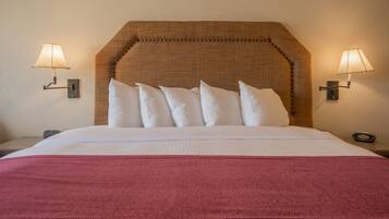 A neatly made bed with a red blanket, a headboard with a textured pattern, and two wall-mounted lamps on either side.