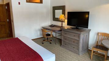 A hotel room with a bed, a desk with a chair, a television, a lamp, and a dresser.