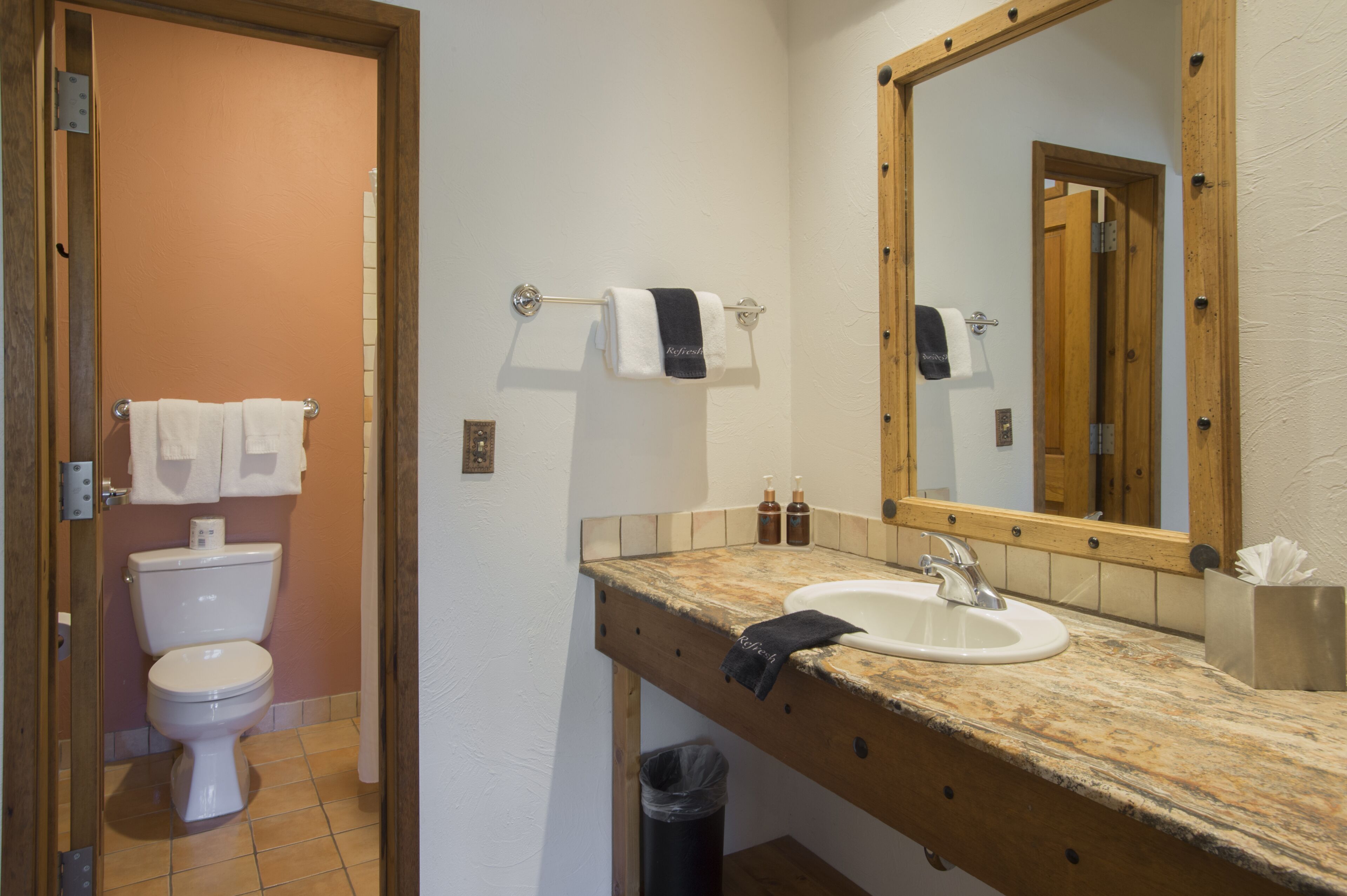 Et badeværelse med toilet, håndvask, spejl og håndklædetørrestativ.