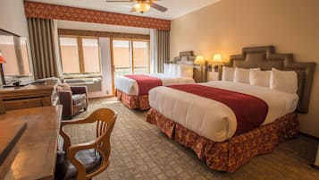 Quarto de hotel com duas camas, uma escrivaninha, uma cadeira, um ventilador de teto e uma janela com cortinas.