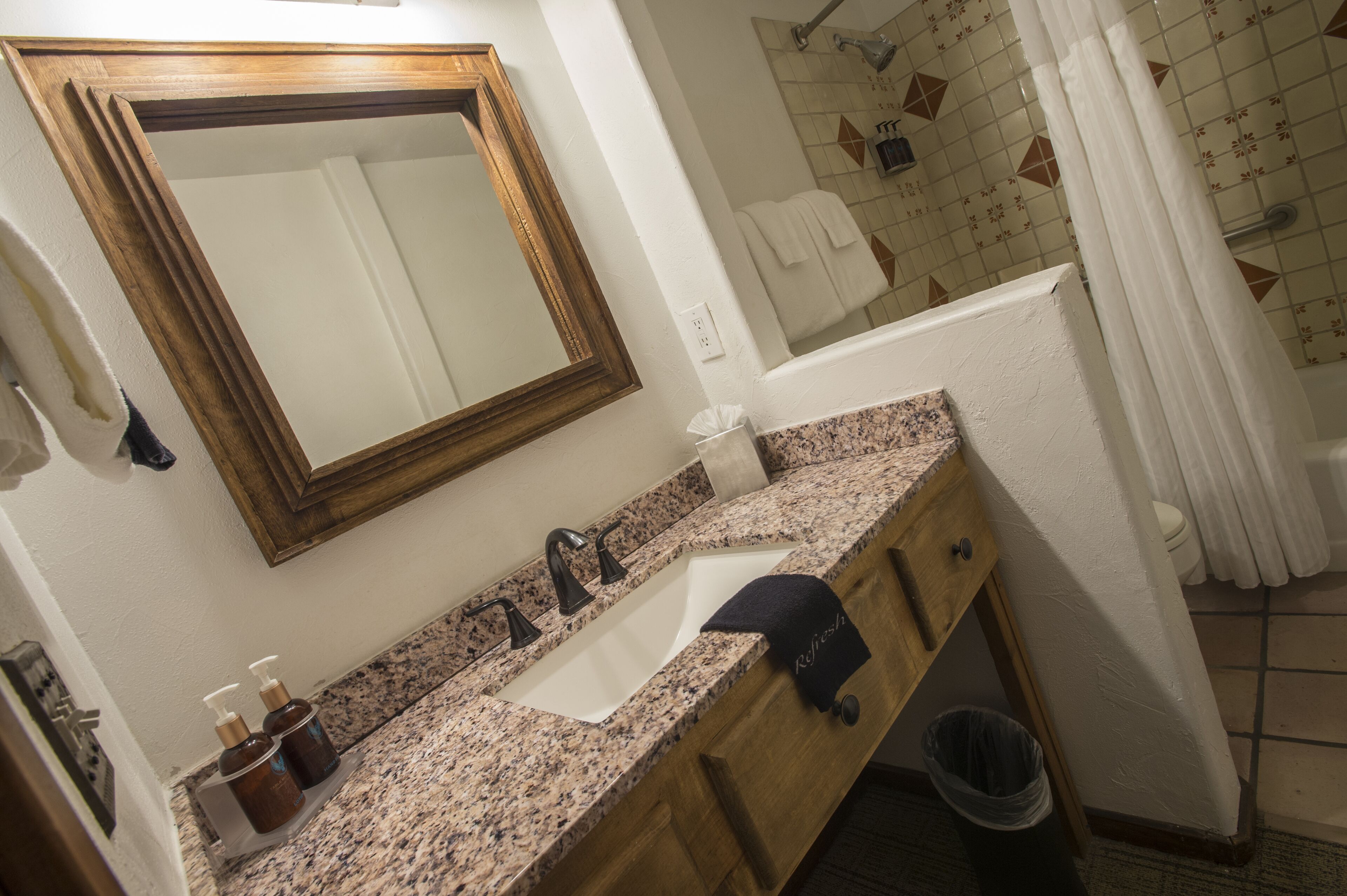 A bathroom with a wooden vanity, a sink, a mirror, and a shower area.