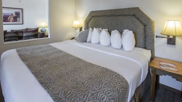Una cama bien hecha con una colcha estampada y un cabecero con botones decorativos. Hay dos lámparas de noche y una mesita con un libro encima.