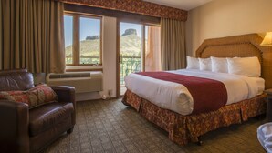 Una habitación de hotel con una cama grande, un sillón de cuero, una ventana con vistas a una colina y un balcón.