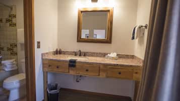 A bathroom with a wooden vanity, a sink, a mirror with lights, a towel rack, and a trash can.