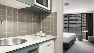 A modern hotel room with a kitchenette, a bed, and a view of a building.