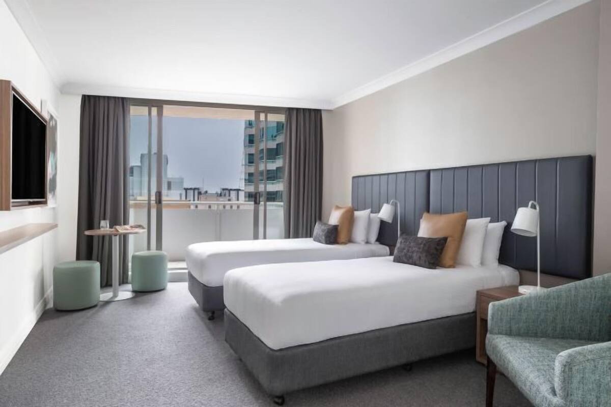 A hotel room with two beds, a TV, a balcony, and a view of the city.