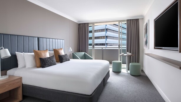 A modern hotel room with a large bed, a desk, a chair, a TV, and a balcony with a city view. - Mantra Chatswood (Chatswood)