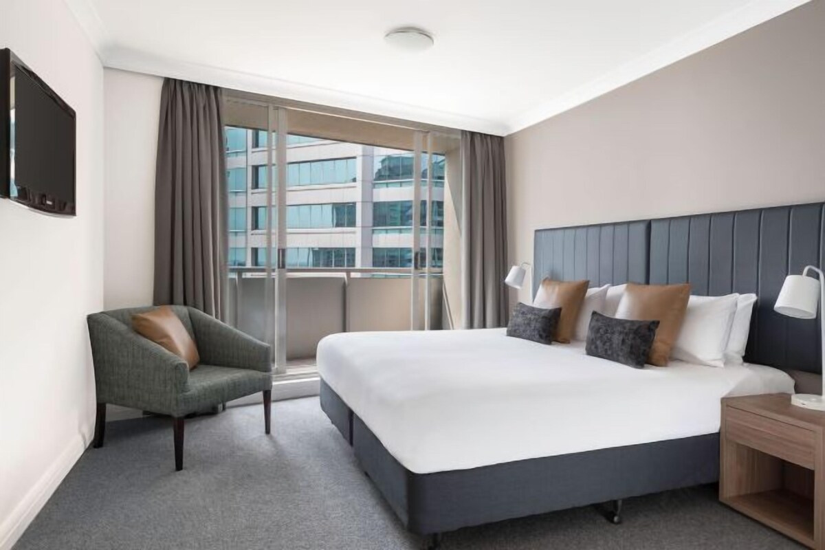 Een hotelkamer met een groot bed, een stoel, een nachtkastje, een televisie en een raam met gordijnen.
