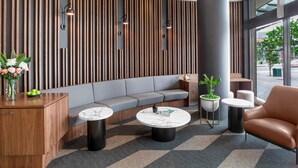 Un vestíbulo moderno con una pared curva de madera, un sofá gris, mesas redondas y un pilar grande.