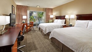 A hotel room with two beds, a desk with a TV, a chair, and a balcony with curtains. - Anaheim Portofino Inn and Suites (Anaheim)